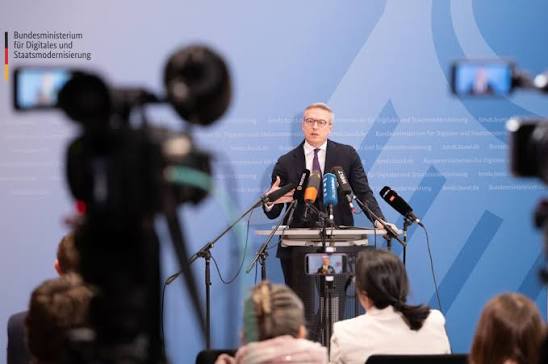 Karsten Wildberger at a lectern at a ministry press conference, cameras in the foreground