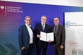 Karsten Wildberger holding a signed document between two men in front of a ministry backdrop