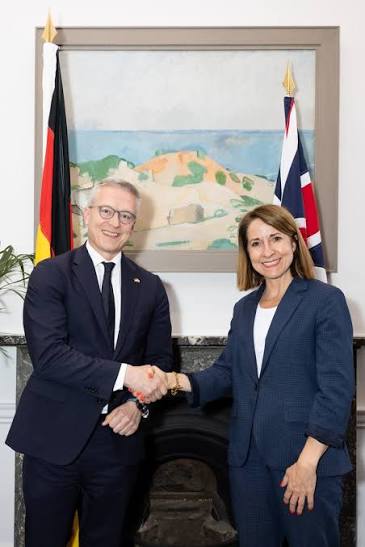 Karsten Wildberger shaking hands with a woman in front of German and British flags