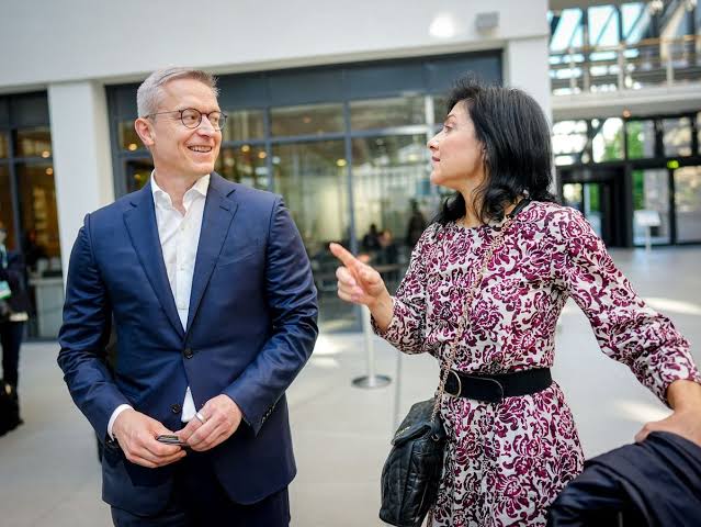Karsten Wildberger in a blue suit listening to a woman in a bright atrium