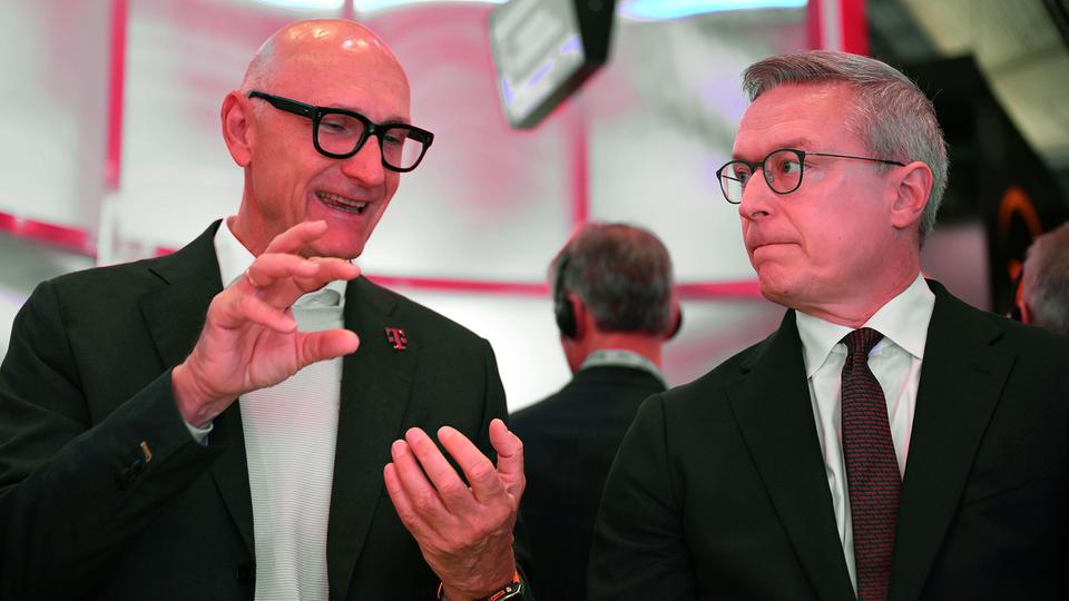 Karsten Wildberger, wearing glasses and a dark suit, listening to Deutsche Telekom chief executive Tim Höttges, who gestures while speaking at an event